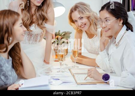 belles filles clients ou modèles assis près de professionnel moderne tailleur, designer de robes de mariage à la mode dans son propre salon, assis sur la table sans Banque D'Images