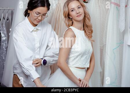 belle femme caucasienne client et tailleur dans la boutique de mariage, prenant des mesures du corps pour la création nouvelle robe, la préparation d'un mariage Banque D'Images