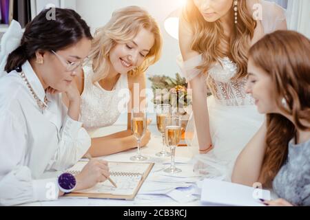 groupe caucasien de femmes se sont rassemblées dans le bureau de designer pour discuter de nouveau style de robe, les jeunes filles dans les robes de mariage blanches tendance Banque D'Images