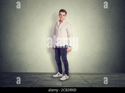 Portrait d'un jeune homme confiant souriant légèrement, debout isolé sur fond gris sol gris en studio. Prise de vue horizontale avec modèle d'espace de copie en W Banque D'Images