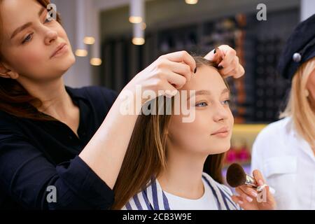 coiffeur caucasien prudent tenant les cheveux du client dans les mains, va couper les bouts de cheveux, faisant la coiffure à la jeune fille client assis sur la chaise oppos Banque D'Images