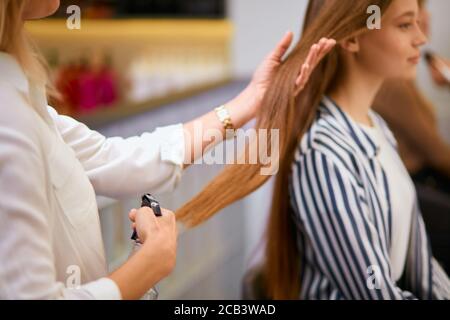 Coiffeur moderne et élégant tidies les cheveux longs du jeune client, en faisant une coiffure la veille des vacances. Transformation complète en salon de beauté Banque D'Images