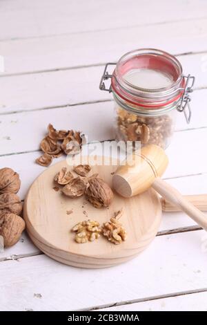 Plan vertical d'un maillet en bois écrasant les coquilles de noyer et noix dans un bocal sur une table blanche Banque D'Images