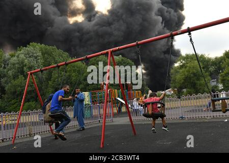 Les gens dans un parc comme la fumée se blère d'un incendie grave sur un domaine industriel à Birmingham. Les équipes de 10 moteurs d'incendie s'attaquent à l'incendie. Banque D'Images