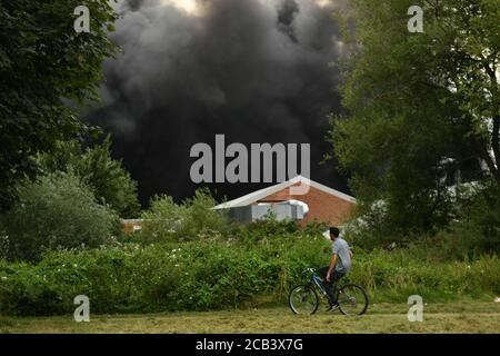 Un homme passe à vélo tandis que la fumée s'illumine d'un feu violent sur un domaine industriel de Birmingham. Les équipes de 10 moteurs d'incendie s'attaquent à l'incendie. Banque D'Images