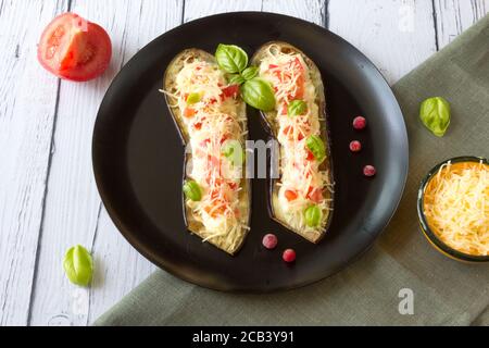 Aubergine frite farcie de tomates, fromage râpé, vinaigrette au yaourt et canneberges, garnie de feuilles de basilic sur une assiette foncée Banque D'Images