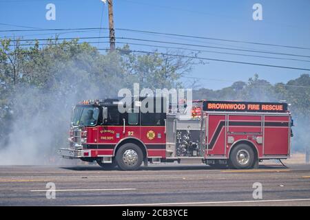 Brownwood, Texas USA-août 10 2020: Camions d'incendie moteurs les combattants éteignent un feu de forêt brumeux sur le bord de la route causé par la litière de cigarette allumée par la sécheresse. Banque D'Images