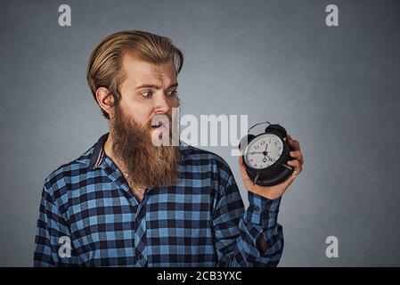 Jeune homme choqué regardant le réveil avec peur d'être en retard. Culotte taille basse avec barbe en tissu à carreaux bleu isolée sur gris gris studio bac Banque D'Images