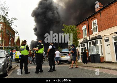 La police et les habitants de la région observent le fait que de la fumée s'échappe d'un incendie violent dans une zone industrielle de Birmingham. Les équipes de 10 moteurs d'incendie s'attaquent à l'incendie. Banque D'Images