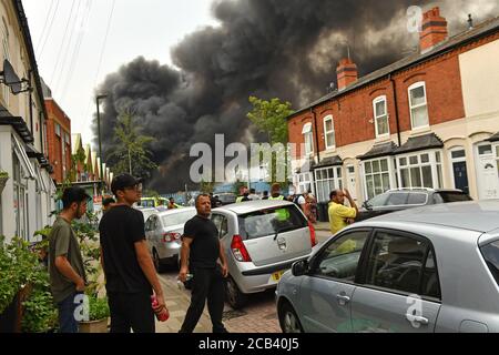 Les habitants de la région observent le fait que de la fumée s'échappe d'un incendie violent dans une zone industrielle de Birmingham. Les équipes de 10 moteurs d'incendie s'attaquent à l'incendie. Banque D'Images