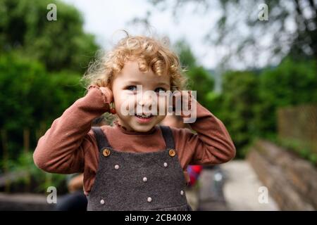 Portrait d'une petite fille debout à la ferme, tenant des boucles d'oreilles en cerisier. Banque D'Images