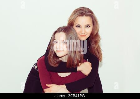 Amour de mère et de fille. Une adolescente et une femme adulte embrassant et regardant l'appareil photo avec le sourire sur fond blanc Banque D'Images