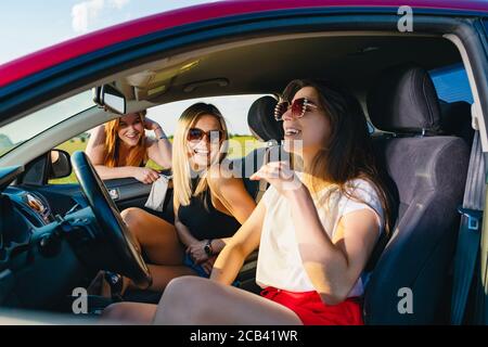 Deux jeunes filles attirantes s'assoient dans un salon de voiture et bavardent avec la troisième derrière la fenêtre, les aventures positives de voyage des femmes. Banque D'Images