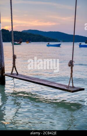 Faites un swing sur la plage de Koh Rong Samloem, Leng Meng Beach (baie de Saracen). Coucher du soleil, bateaux et collines en arrière-plan. Banque D'Images