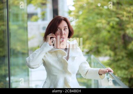 Femme d'âge moderne avec tenue blanche ayant un appel téléphonique avec un grand plaisir sur la terrasse Banque D'Images