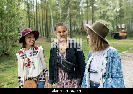 Positive jeunes femmes interraciales dans les vêtements hippie marchant ensemble pendant vacances au camping Banque D'Images