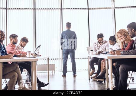 Un chef d'équipe réussi est en train de préparer un plan tandis que ses collègues sont concentrés sur le travail. Le patron regarde à travers la fenêtre pendant que ses employés sont s Banque D'Images