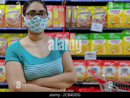 Un client qui se tient devant des tablettes empilées avec des aliments Articles dans un magasin du ministère pendant la pandémie du virus Corona (Covid-19) porter un masque en coton Banque D'Images