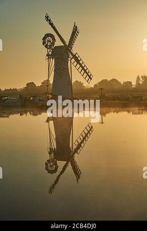Le moulin à vent de drainage Thurne Dyke Norfolk, se reflète dans la rivière Thurne au lever du soleil avec des bateaux amarrés à la rive de la rivière. Banque D'Images