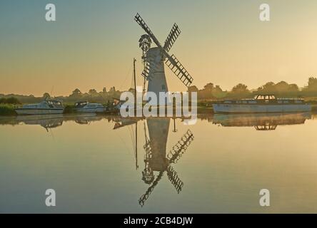 Le moulin à vent de drainage Thurne Dyke Norfolk, se reflète dans la rivière Thurne au lever du soleil avec des bateaux amarrés à la rive de la rivière. Banque D'Images