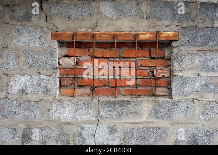 La fenêtre du sous-sol est recouverte de briques rouges et une grille est installée. Mur gris avec de grandes briques et un grill en métal sur la fenêtre. Intrusio Banque D'Images