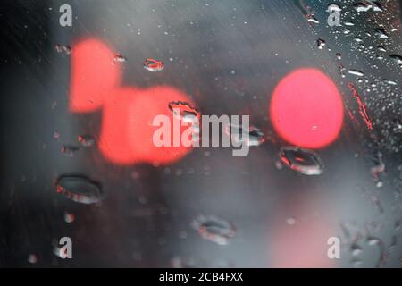 Gros plan de verre avec gouttes de pluie et réflexions de lumière, gouttes d'eau sur le verre de voiture, mise au point sélective Banque D'Images