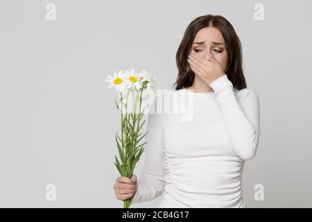 Studio portrait de la femelle couvrant son nez, ayant une réaction allergique aux fleurs - camomille, isolé. Allergie. Banque D'Images