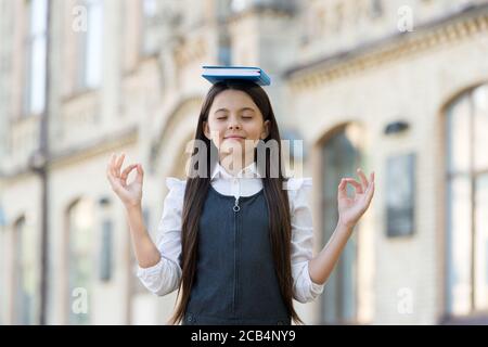 Calme l'esprit. Un petit enfant fait de la méditation à l'extérieur. Petite fille ne mudra mains tenant le livre sur la tête. Méditation pour l'équilibre mental. Cours de méditation pour débutant. École et éducation. Meilleure thérapie. Banque D'Images