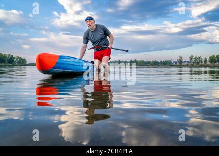 Le pagayer debout masculin senior lance son pagaleboard sur un lac pour une séance d'entraînement matinale dans le nord du Colorado, pagayer en solo comme une forme de dista sociale Banque D'Images