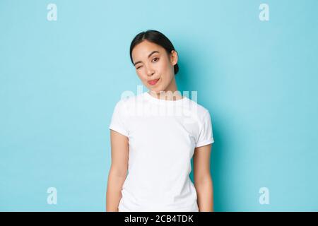 Portrait de la sassy et attrayante fille asiatique en blanc décontracté t-shirt, montrant la langue et le wencing coquettish, regardant l'audace à la caméra en se tenant Banque D'Images