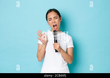 Concept de style de vie, de personnes et de loisirs. Insouciante, belle fille asiatique chantant dans le microphone avec une expression passionnée, des yeux proches et des gestes Banque D'Images