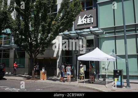 Les Shoppers masqués font la queue et suivent les conseils d'un assistant-boutique avant d'entrer dans un magasin de détail REI rouvert à Portland, en Oregon, en été pandémique. Banque D'Images