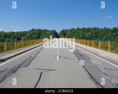 route asphaltée sur pont avec barrière jaune et arbres verts en arrière-plan, ciel bleu clair Banque D'Images