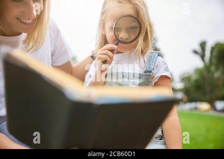 Petite fille mignonne regardant à travers la loupe dans le stationnement Banque D'Images