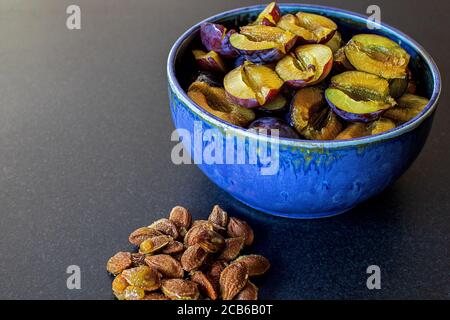 un tas de prunes juteuses piquées dans un bol en céramique fait maison. les pierres se trouvent sur le comptoir de la cuisine Banque D'Images