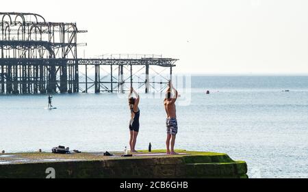 Brighton Royaume-Uni 11 août 2020 - ce couple profitez du yoga par temps chaud sur la plage de Brighton un autre jour ensoleillé que les températures devraient atteindre à nouveau bien au-dessus de 30 degrés dans certaines parties du Sud-est tandis que d'autres parties du pays sont touchées par les tempêtes de tonnerre : Credit Simon Dack / Alamy Live News Banque D'Images