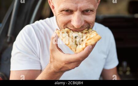 Portrait en gros plan de l'homme qui mange de la pizza. Un gars vêtu d'un T-shirt blanc Banque D'Images