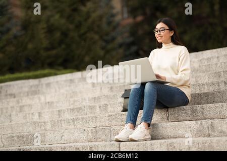 Etudiant dans les spécifications à l'aide d'un ordinateur portable, assis sur des marches Banque D'Images