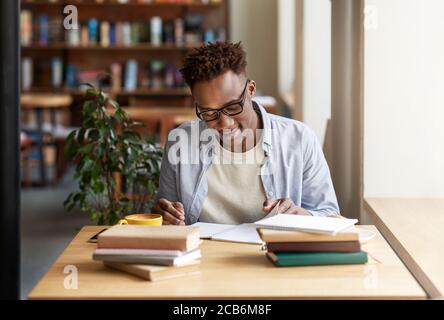 Joyeux homme noir étudiant ou travaillant avec des livres au café boutique Banque D'Images