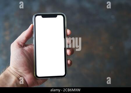 Kaliningrad, Russie - 08.08.2020: Un jeune homme tient dans la main un smartphone moderne avec un écran blanc sur fond sombre. Maquette Banque D'Images