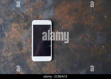 Téléphone blanc avec écran cassé sur fond sombre Banque D'Images