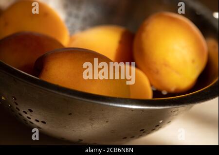 Abricots mûrs juteux dans une passoire en métal sur une table en bois clair au soleil. Gros plan Banque D'Images