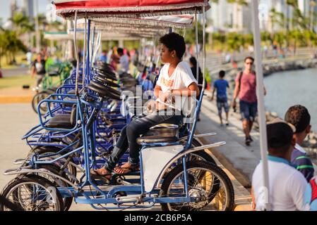 Panama City / Panama - 25 mars 2016: Femme panaméenne avec les cheveux bouclés assis sur des voitures à pédales à côté de la promenade avec des gens qui se baladant Banque D'Images