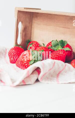 Vertical, gros plan, fraises fraîches de couleur rouge vif, dans une boîte en bois rustique à côté d'un tissu, prêtes à manger. Mise au point sélective Banque D'Images