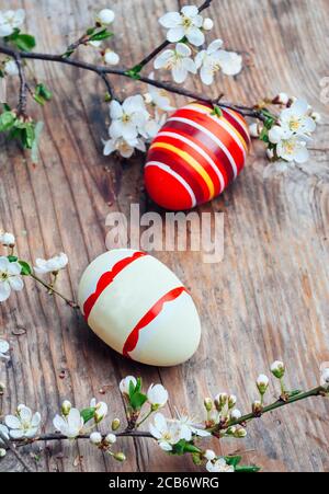 Vue imprenable sur les œufs de pâques peints en couleurs et le décor aux branches en fleur de cerisier sur une table en bois d'époque. Les vacances saisonnières traditionnelles sont encore plus belles. Banque D'Images