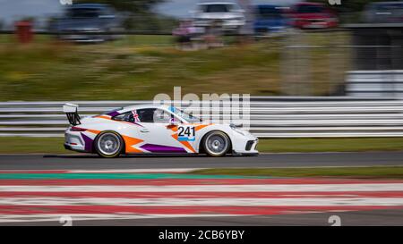 Une photo panoramique d'une voiture de course blanche, orange et pourpre qui fait le circuit d'une piste. Banque D'Images