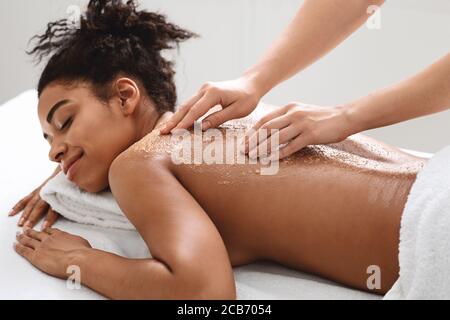 Spa thérapeute frottant la peau noire de la femme, en utilisant des produits de beauté naturels Banque D'Images