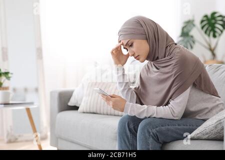 Bouleverser Arab Girl dans hijab regardant l'écran de smartphone à la maison Banque D'Images