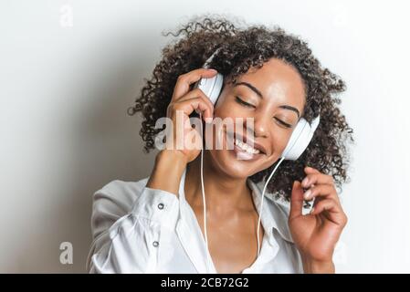 belle femme afro-américaine souriante profitant de la musique avec des écouteurs blancs Banque D'Images