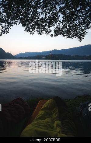 Début de matinée lac Bled en Slovénie. Lac calme, soleil levant derrière les montagnes, Alpes. Sacs de couchage en premier plan, aventure en plein air dans le Trigl Banque D'Images